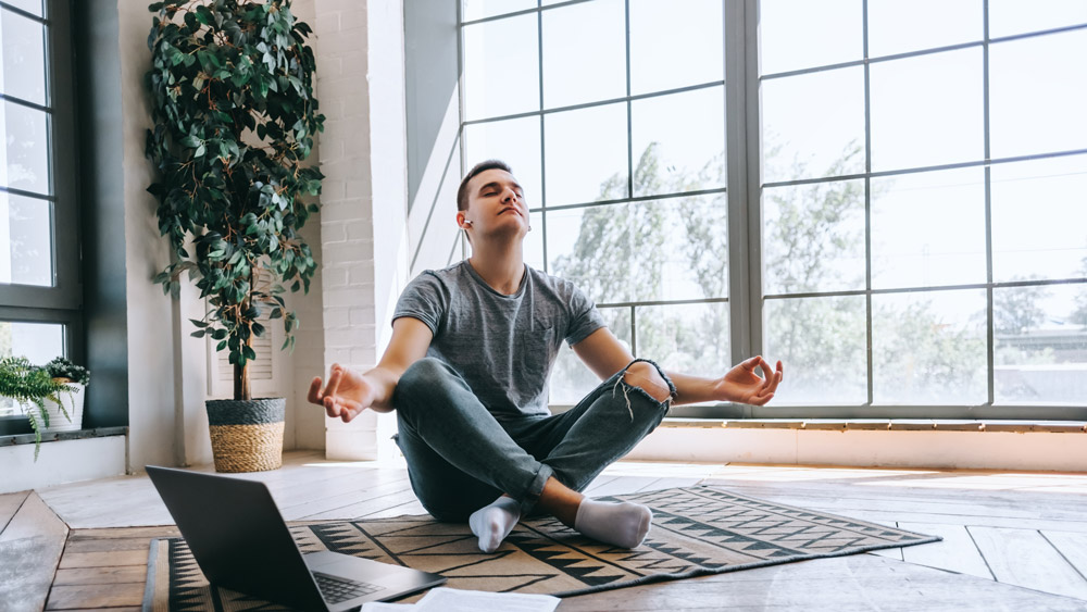 Pleased and relaxed man sits crossed leg doing meditation