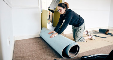 Woman rolling up old carpet in preparation to renovate it