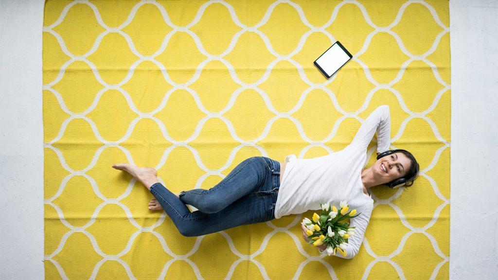 A woman lied down on yellow carpet while listening to music