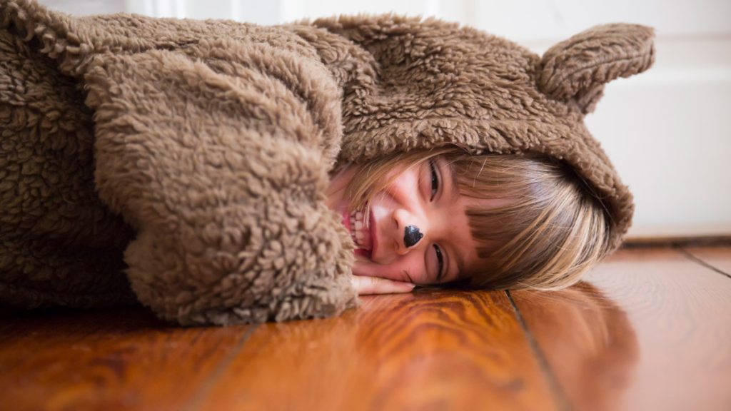 Laughing little girl in bear custom lying down on laminate flooring