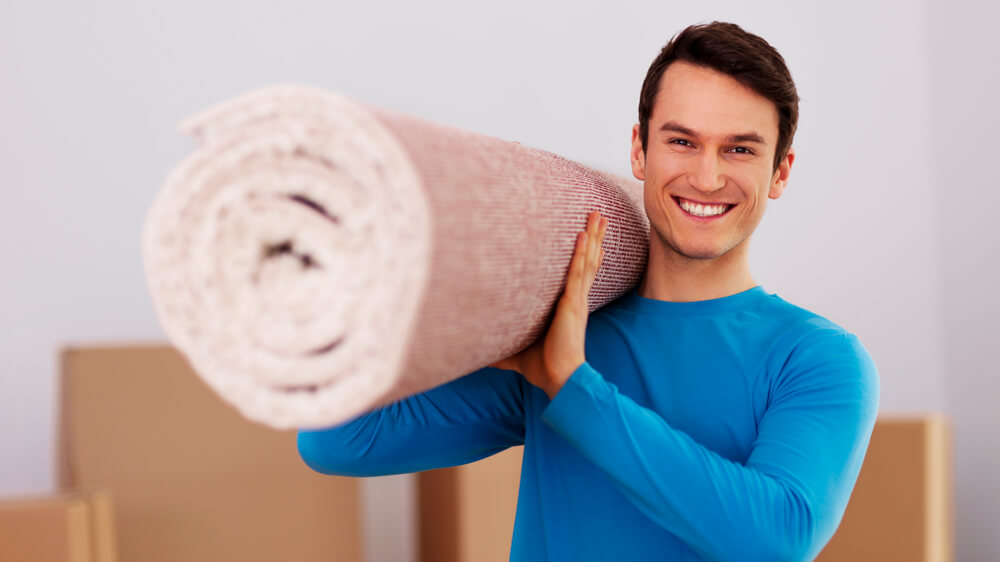 Happy cleaning professional man carrying a carpet