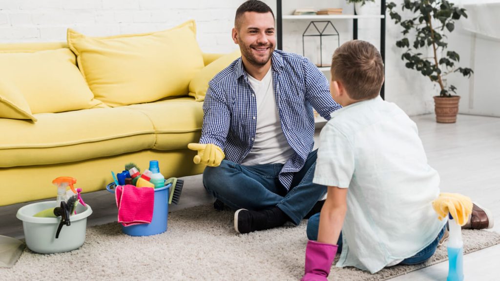 Happy father talking to his son while cleaning carpet