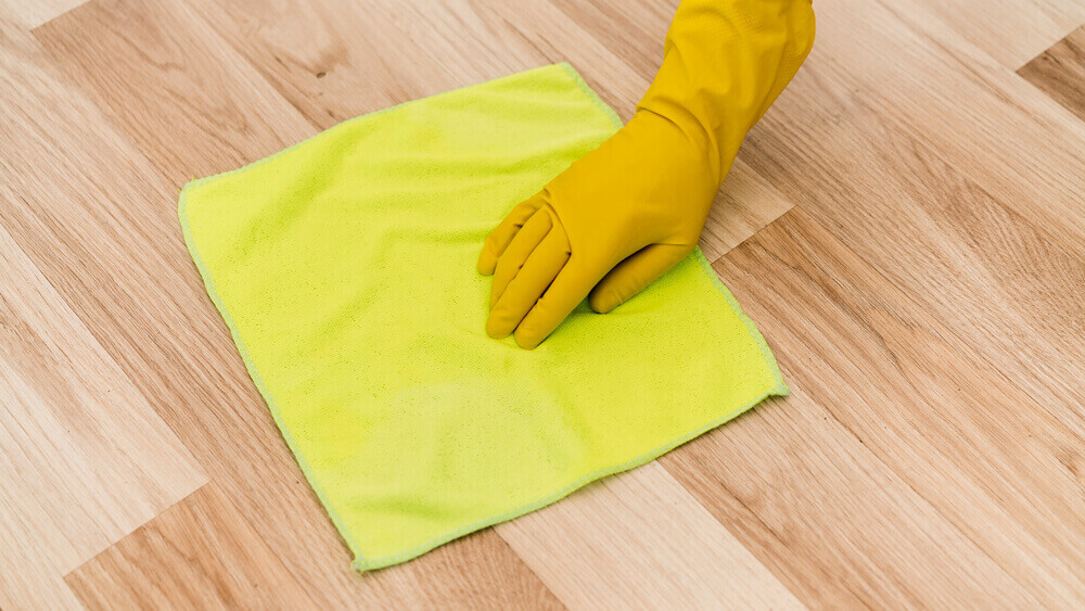 Woman with rubber gloves and dry mop cleaning the laminate flooring