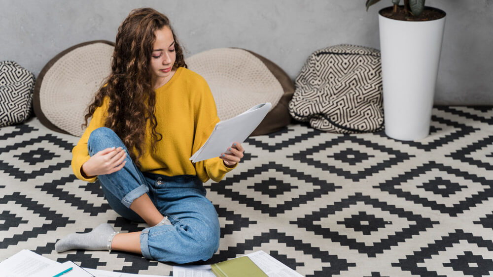 Teenage girl studying at her room floored with patterned carpet