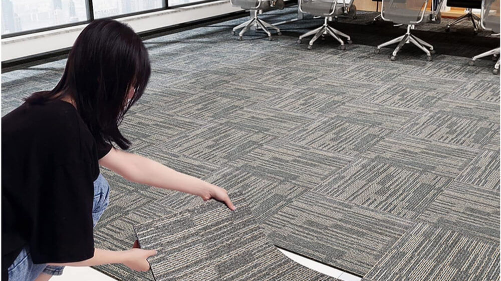 A woman installing carpet tiles in an office