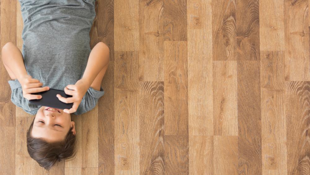 Young boy playing smartphone on laminate flooring