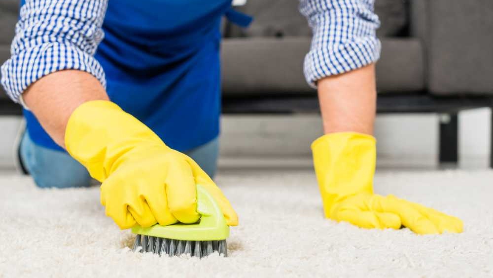 Close-up of man cleaning carpet with yellow plastic gloves and a brush